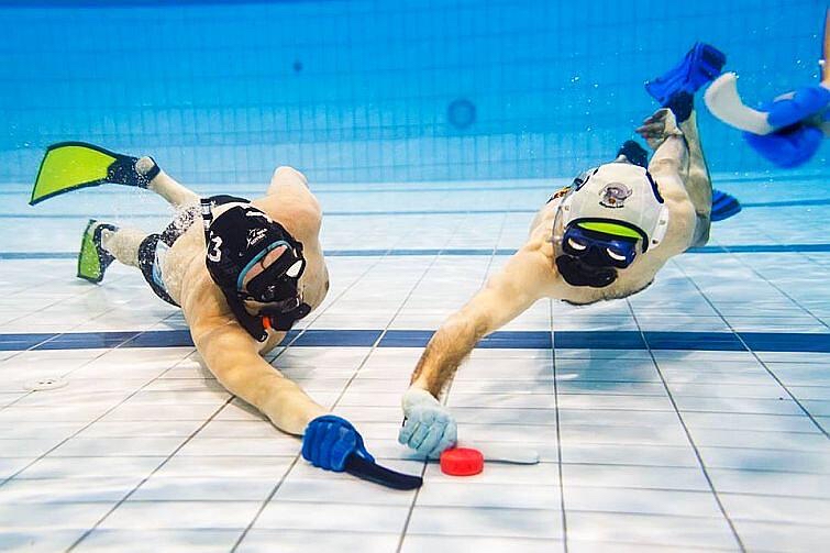 Two underwater hockey players competing for the puck